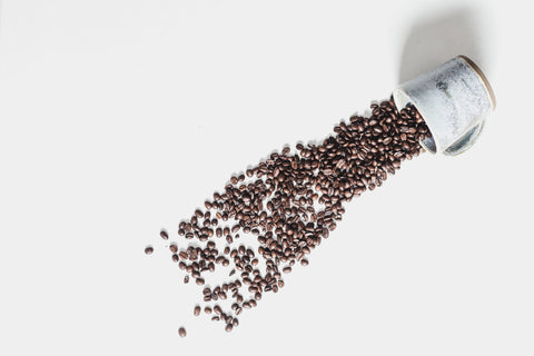 Glass jar tipped over with coffee beans spilling out on a white background
